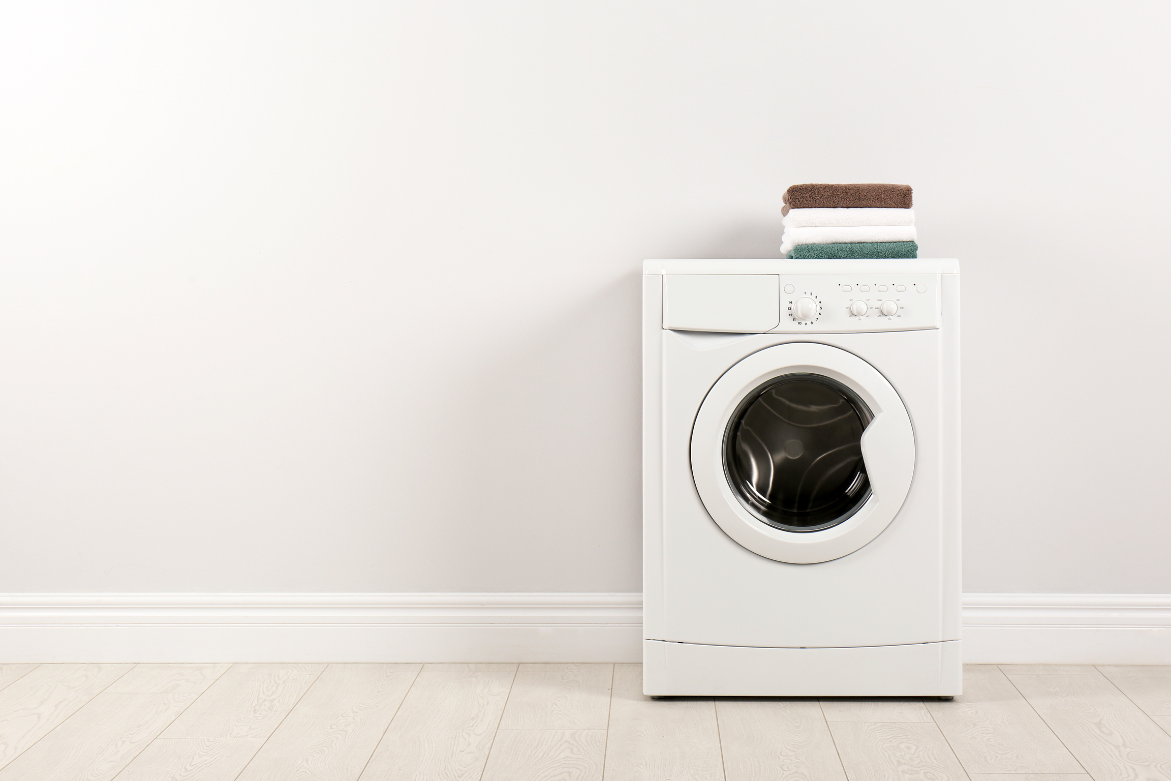 Modern Washing Machine with Stack of Towels near White Wall, Spa
